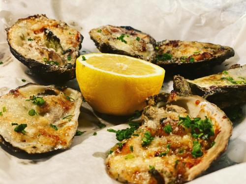 Grilled oysters topped with herbs, served with a lemon wedge on parchment paper.