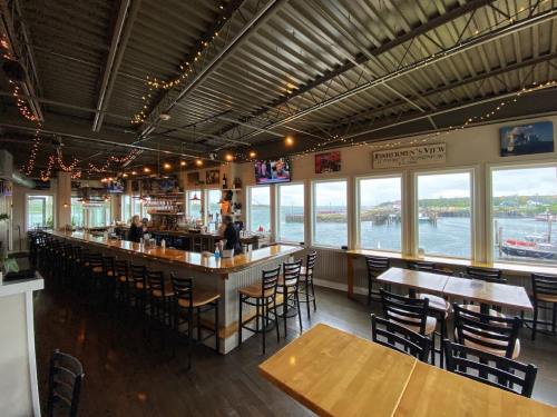 Interior of a restaurant with a bar, tables, and large windows overlooking a waterfront view. Warm lighting and decor visible.