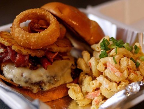 A juicy burger topped with bacon, cheese, and onion rings, served with a side of macaroni salad.