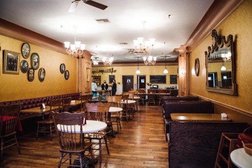 A cozy restaurant interior with wooden tables, chairs, vintage decor, and warm lighting.