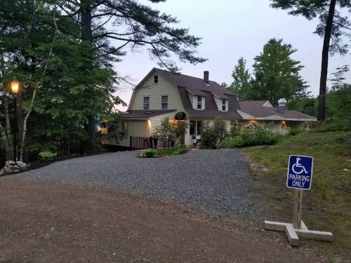 A large house surrounded by trees, with a gravel driveway and a sign indicating accessible parking.