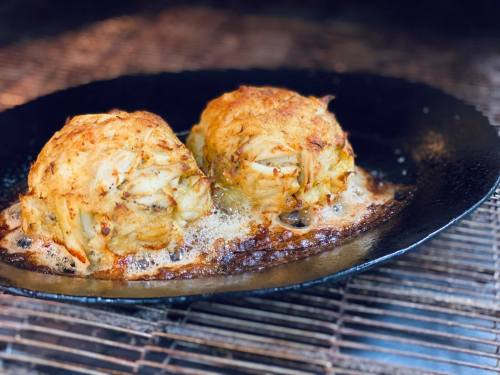 Two golden-brown crab cakes sizzling in a cast iron skillet, with a crispy exterior and bubbling butter underneath.