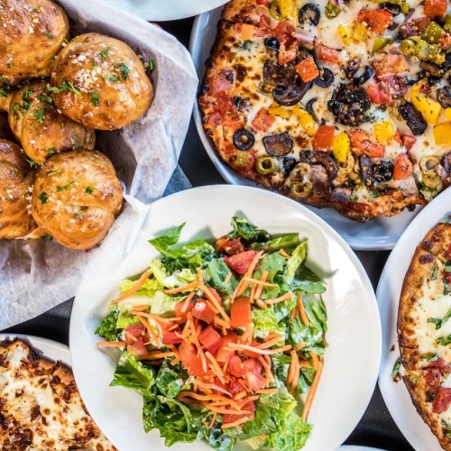 A spread of delicious food including pizza, salad, and garlic knots on white plates.