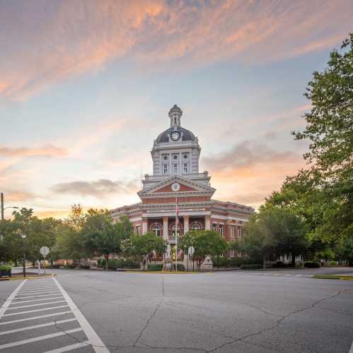 Historic courthouse with a clock tower, surrounded by trees, under a colorful sunset sky.