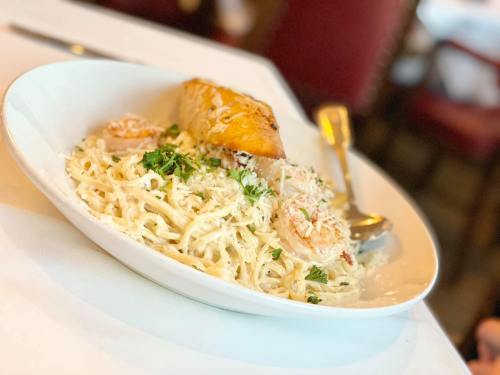 A plate of creamy pasta with shrimp, garnished with parsley and served with a slice of garlic bread.