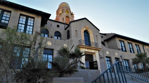 Historic building with a decorative dome, featuring large windows and palm trees in the foreground.