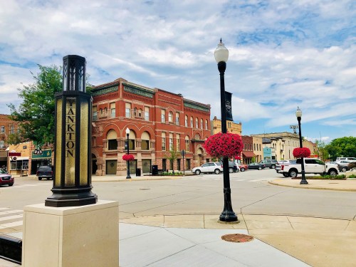A street view of a small town with historic buildings, decorative flower baskets, and a cloudy sky.