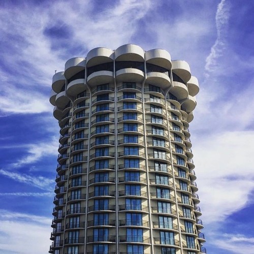 A tall, modern building with a rounded top and numerous windows, set against a blue sky with wispy clouds.