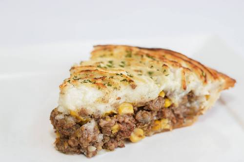 A slice of shepherd's pie with a golden crust, filled with ground meat and corn, garnished with herbs.