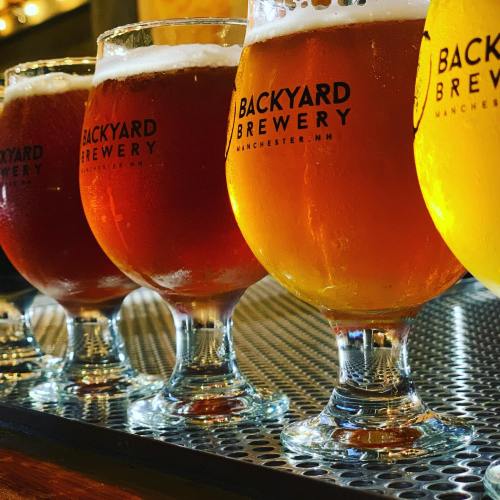 Four glasses of craft beer in varying shades, lined up on a bar with the logo "Backyard Brewery" visible.