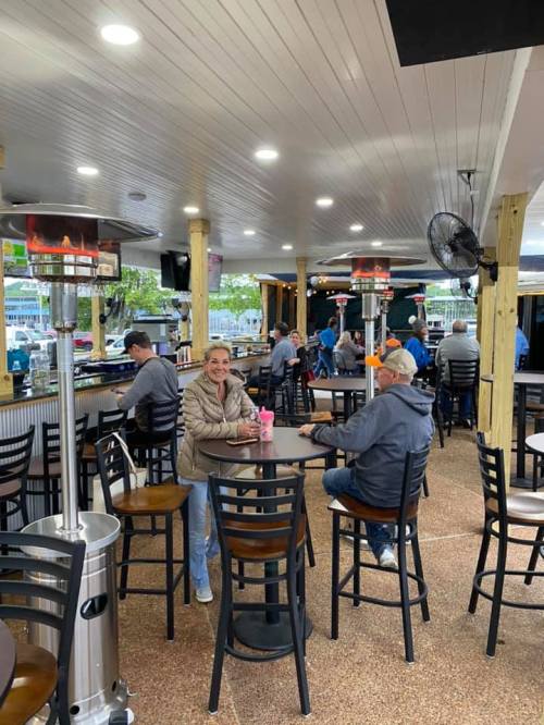A cozy outdoor bar area with patrons seated at tables, enjoying drinks and conversation under heating lamps.