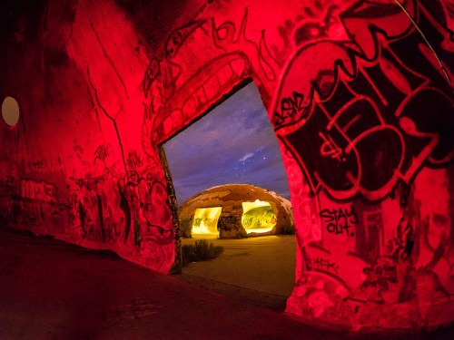 A brightly lit, graffiti-covered tunnel opens to a starry sky, illuminated in red hues.