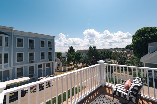 View from a balcony overlooking a sunny neighborhood with trees and clouds in the sky.