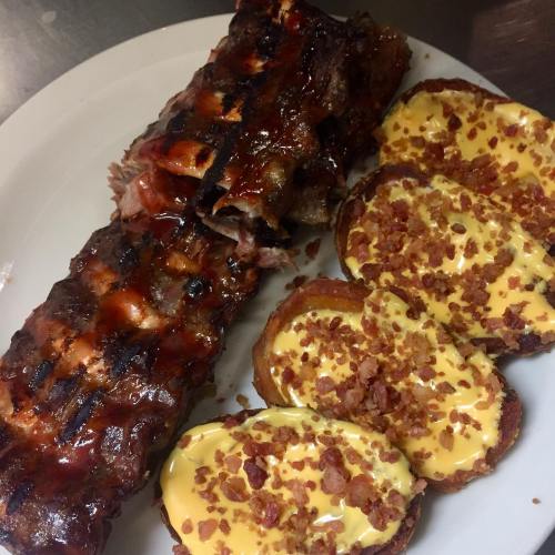 A plate featuring grilled ribs glazed with barbecue sauce and crispy potato slices topped with cheese and bacon bits.