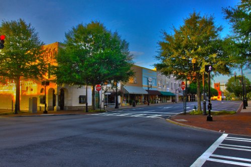 A quiet street scene with trees, shops, and traffic lights under a blue sky at dusk.