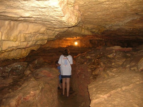A person exploring a rocky cave with soft lighting illuminating the path ahead.