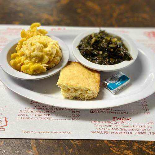 A plate with macaroni and cheese, collard greens, cornbread, and a butter packet on a menu backdrop.