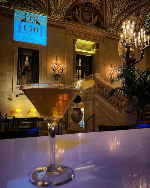 A martini glass in the foreground with an elegant, ornate interior and a projection reading "150" in the background.