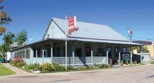 A charming blue restaurant with a metal roof, surrounded by greenery and a clear blue sky.