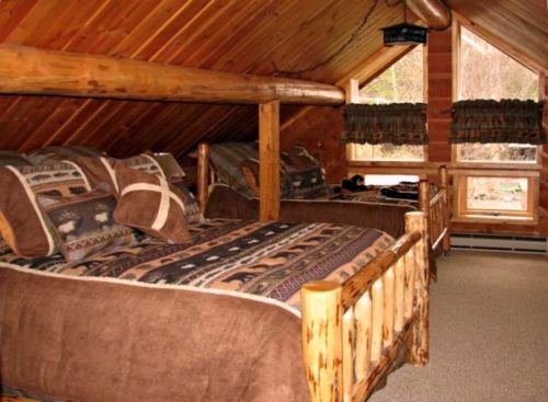 Cozy wooden cabin interior with two beds, rustic decor, and large windows letting in natural light.
