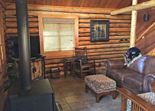 Cozy log cabin interior with wooden walls, a leather sofa, a rocking chair, and a wood stove.