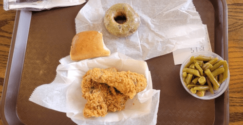 A tray with fried chicken, a roll, green beans, and a donut on a paper-lined surface.