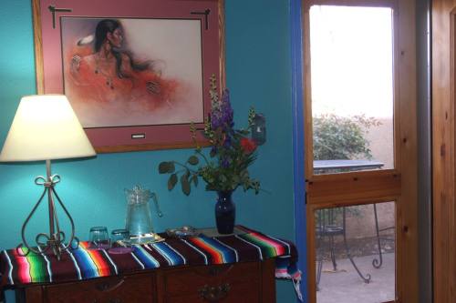 A cozy room with a colorful table runner, a lamp, a vase of flowers, and a painting on the wall, next to a door.