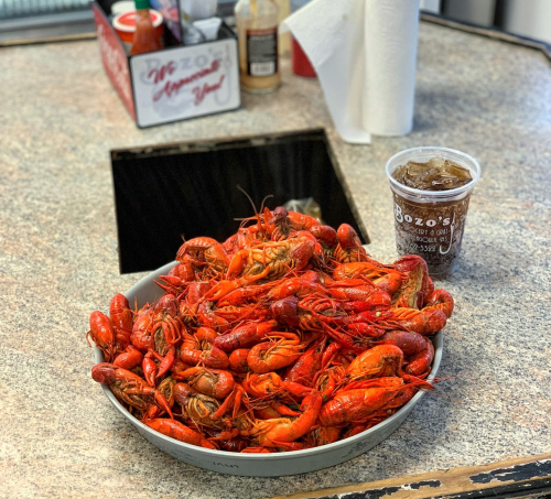 A large bowl of bright red crawfish on a countertop, next to a cup of iced drink.