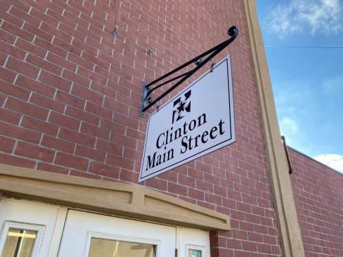 Sign for "Clinton Main Street" mounted on a brick wall, with a clear blue sky in the background.