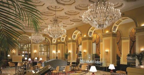 Elegant hotel lobby featuring ornate chandeliers, plush seating, and decorative arches with lush greenery.