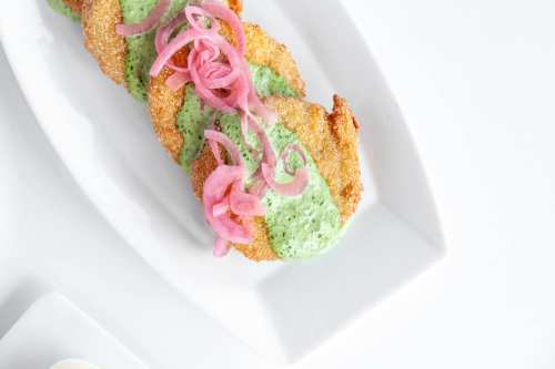 Crispy fried patties topped with green sauce and pickled onions, served on a white plate.