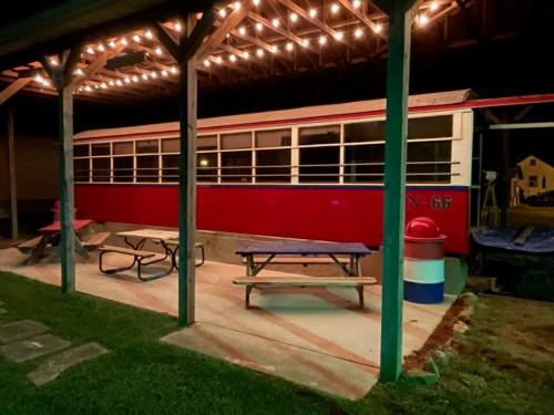 A red train car converted into a dining area, illuminated by string lights, with picnic tables underneath a shelter.