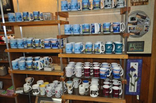 A display of various mugs on wooden shelves, featuring different designs and colors.