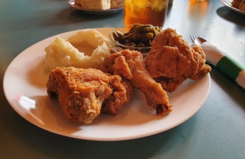 A plate of fried chicken, mashed potatoes, and green beans, with a drink in the background.