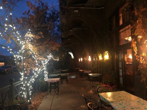 A cozy outdoor dining area with illuminated trees and tables, set against a darkening evening sky.