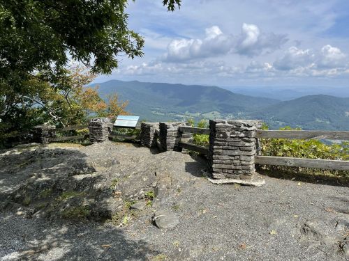 Scenic overlook with stone barriers, featuring mountains and a cloudy sky in the background.