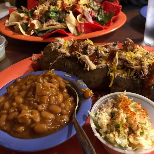 A plate featuring a loaded baked potato topped with meat and cheese, alongside a side of baked beans and coleslaw.