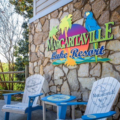 Sign for Margaritaville Lake Resort on a stone wall, with two white chairs in front and tropical decor.