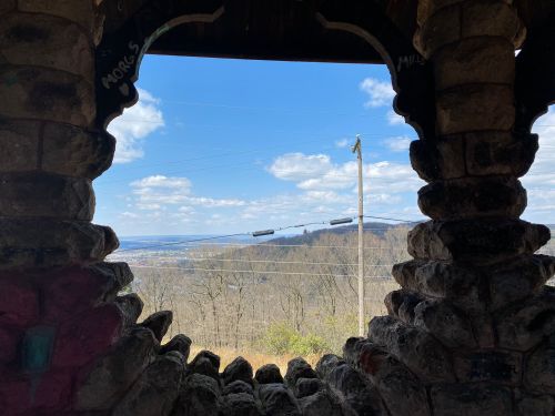 View from a stone archway overlooking a valley with trees and a blue sky dotted with clouds.