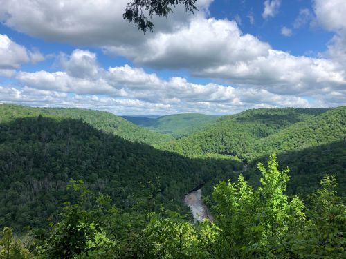 Lush green hills under a blue sky with fluffy clouds, overlooking a winding river in a serene landscape.