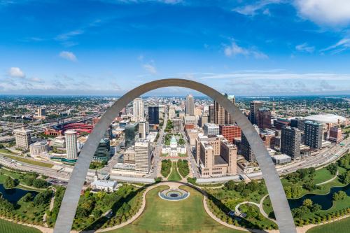 Aerial view of St. Louis with the Gateway Arch framing the city skyline and green parks below.