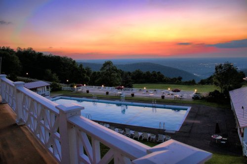 A serene sunset over a pool with lounge chairs, surrounded by lush hills and a clear sky.