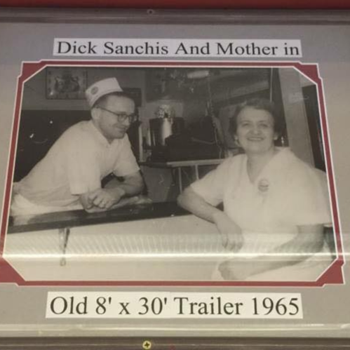Black and white photo of a man and woman in a trailer, labeled "Dick Sanchis and Mother in Old 8' x 30' Trailer 1965."