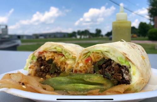 A close-up of a burrito filled with rice, beef, and vegetables, served with grilled peppers and a squeeze bottle of sauce.