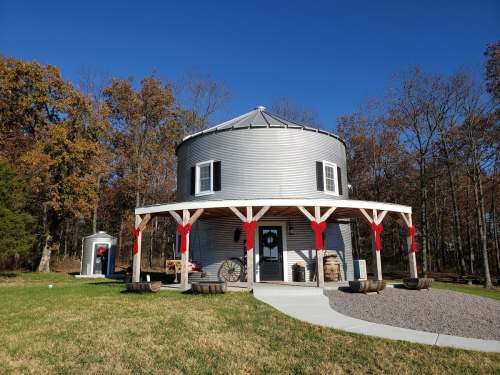 A round, silver silo-style building with a porch, surrounded by trees and decorated with red bows for the holidays.