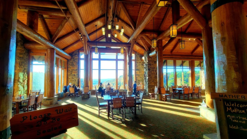 A spacious lodge interior with wooden beams, large windows, and tables, offering a scenic view of the outdoors.