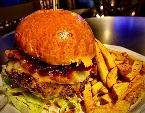 A juicy burger with melted cheese, barbecue sauce, and lettuce, served with golden fries on a plate.