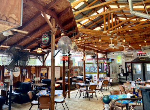 A rustic restaurant interior with wooden beams, fans, and tables, featuring a casual, inviting atmosphere.