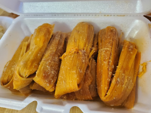 A container filled with several orange-hued tamales wrapped in corn husks.