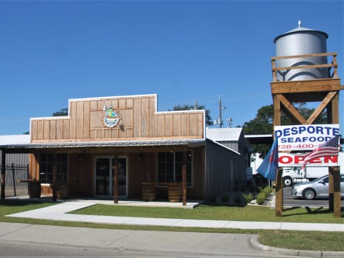 A wooden seafood restaurant with a water tower sign, featuring an "Open" banner and a clear blue sky.